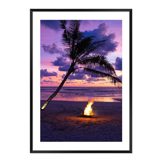 Framed photo of a fire pit by a palm tree on a beach with a sunset sky.