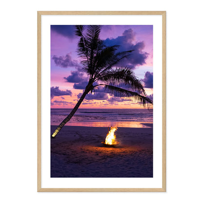 Framed photo of a fire pit by a palm tree on a beach with a sunset sky.