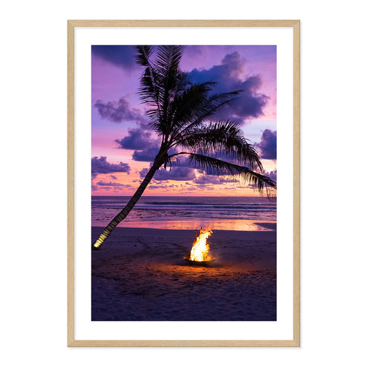 Framed photo of a fire pit by a palm tree on a beach with a sunset sky.