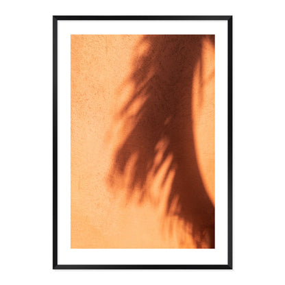 Framed artwork of a palm leaf shadow on a textured terracotta wall.