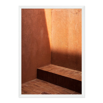 Wooden bench against a textured brown wall with a white frame.