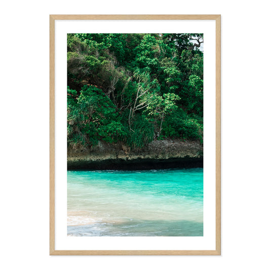 Framed artwork of a tropical landscape with greenery and turquoise water.